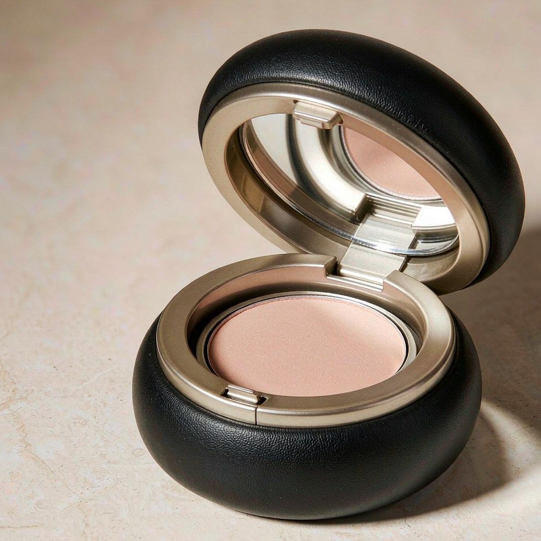 Luxury powder compact in matte black with champagne gold rim, opened